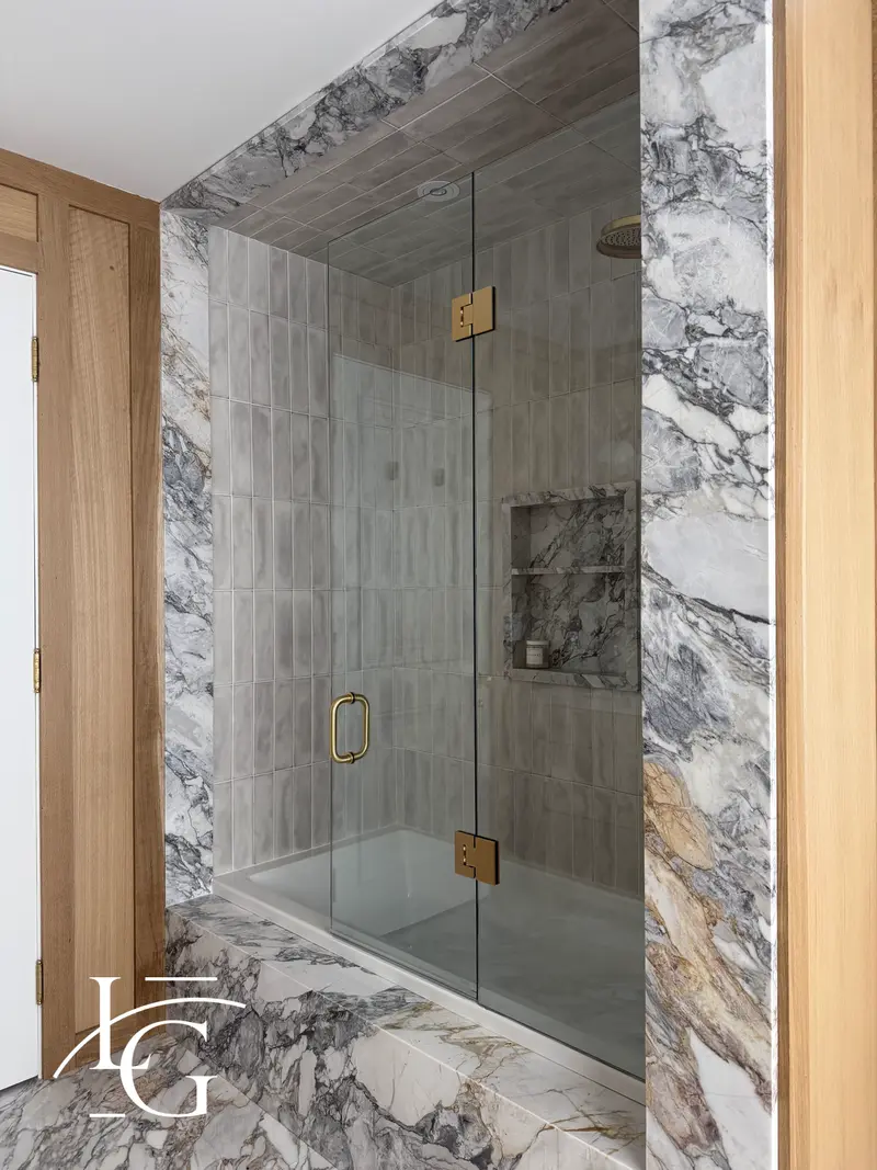 Glass tub door with brass hardware in a marble alcove