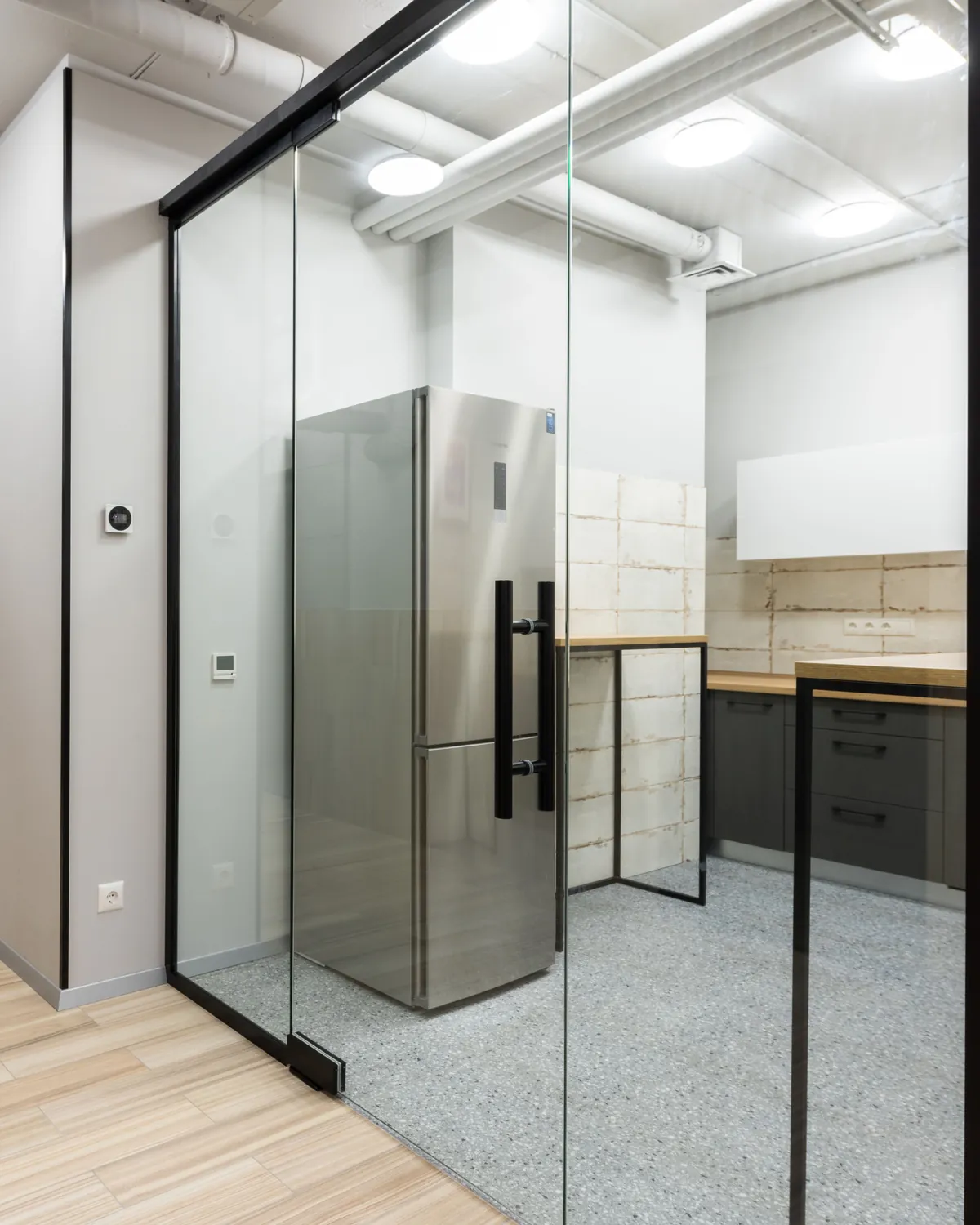 Frameless glass swing door with a long black pull handle closing off an office kitchenette