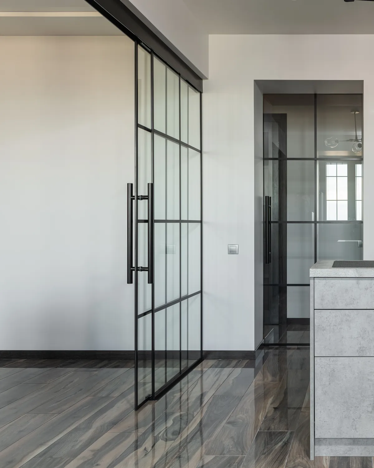 Black-framed glass sliding door running on a ceiling-mounted top track, partly open beside a second glass panel